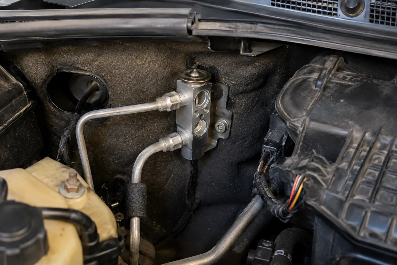 Block-type car A/C expansion valve installed near the firewall in a passenger car engine bay