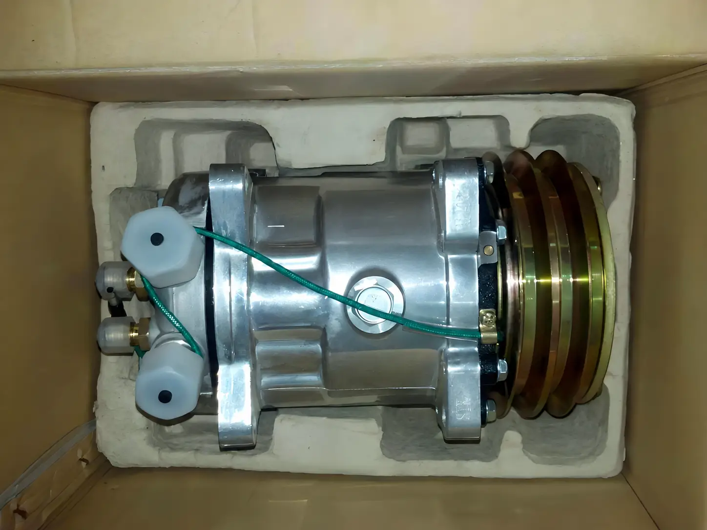 Auto AC compressor packed in a carton with a moulded protective insert, refrigerant ports capped for shipping